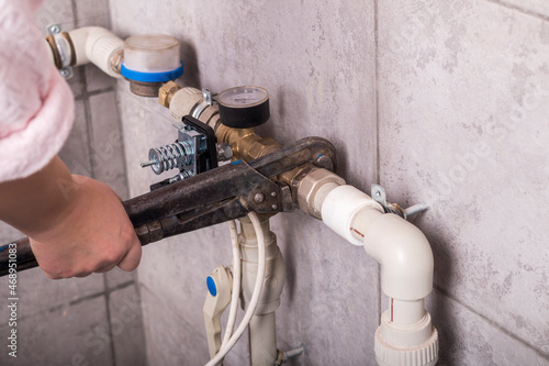 on the wall covered with tiles, there is a pipe with water. a woman in a bathrobe tries to turn it off with a big dirty key. concept of payment of camunal payments