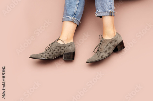 Tableau sur Toile Woman's Caucasian legs in blue twisted jeans and gray suede English brogue Oxfords shoes isolated on light pink beige background
