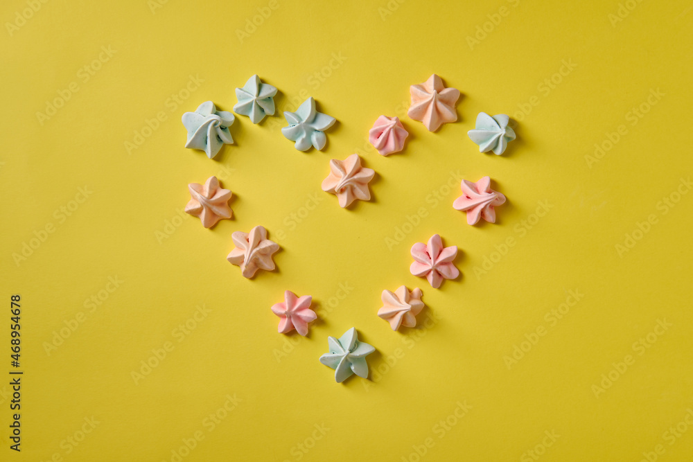 Multicolored meringue on a yellow background in the form of a heart, top view Multicolored meringue on a yellow background in the form of a heart, top view