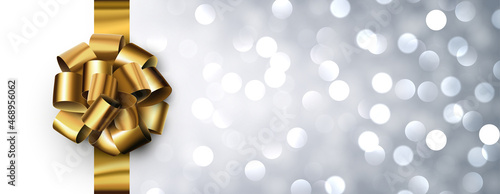 Golden foil ribbon with beautiful bow on silver bokeh background.