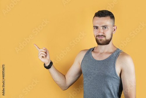 Young man with a beard on a yellow background smiles and points his finger at something, advertising goods on an orange background. Blank for advertising with a man