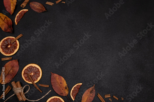 Autumn dark background with candied, dried oranges, cinnamon and spices with red autumn leaves on a black matte background. Top view flat lay background with copy space.