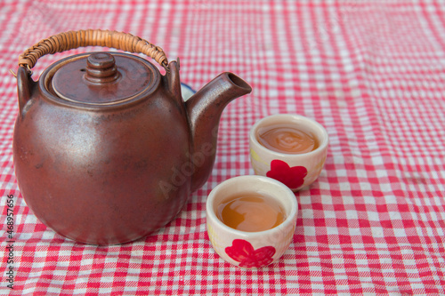 Top views reddish-brown ceramic teapot has two white ceramic tea cups placed on front. On table covered with red cloth , Concept tea for morning health, Natural tea set