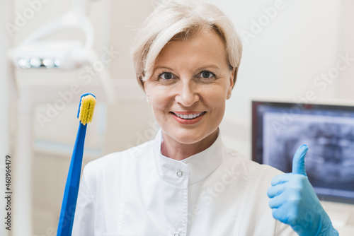 Caucasian mature orthodontist stomatologist smiling showing teaching learning how to use tooth brush correctly showing thumb up in dental stomatological clinic hospital