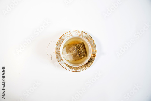 Vista aérea de sumergir una bolsita de té de manzanilla en una pequeña taza de té con adornos dorados sobre un fondo blanco. photo