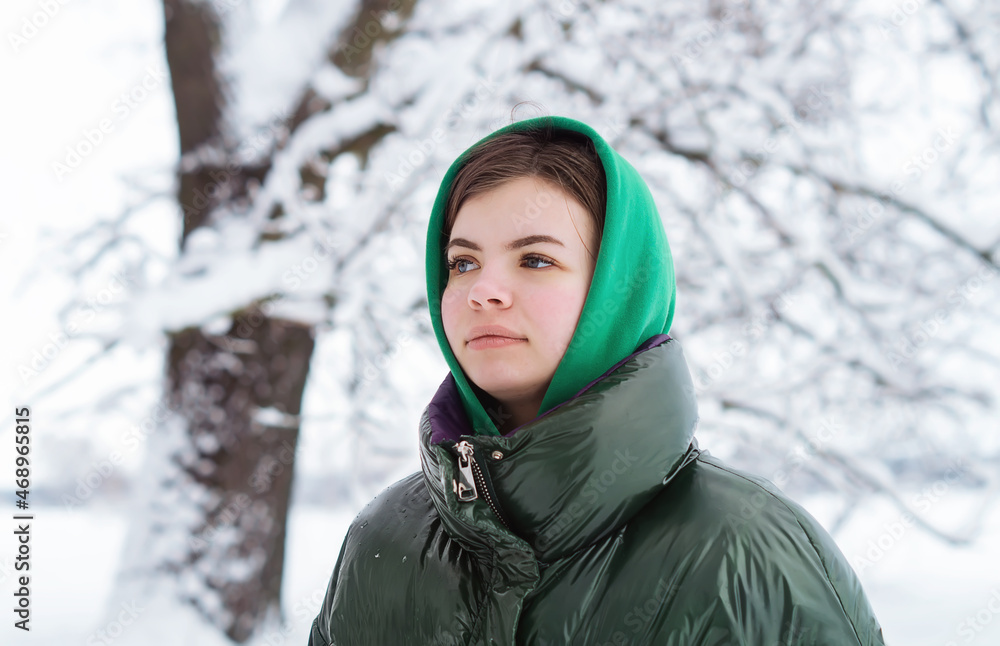 A pretty young teenage girl 18 years old in winter in a snowy forest looks into the distance, enjoying nature. Winter Photo of a beautiful young Belarusian girl. Happy young woman in winter outdoors