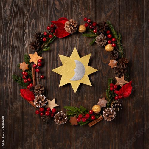 Winter solstice day, December 21. Sun and moon symbol, Christmas trees, pine cones, paddub branches with red berries, candle on dark wooden background, top view. photo