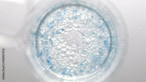 Crystals of blue salt fall down from test tube into clear liquid in flask creating different sized bursting bubbles on light grey background | Mineral skin care cosmetics formulation concept photo