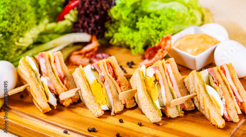 Club sandwiches with egg, ham, bacon, vegetables on wooden cutting board
