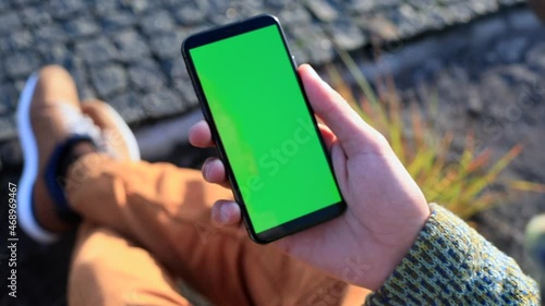 Young man hand holding smartphone with blank green screen. Sunset sunlight rising on background. Businessman freelance lifestyle. Chroma key display. Traveling app online. Network communication. 