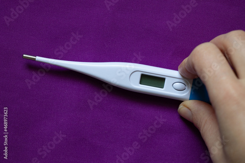 female hand holds an electronic thermometer lies on a purple background, medicine and pharmacy, health and treatment, temperature photo