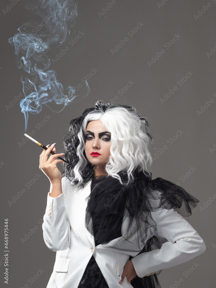 A fatal beauty in a daring fashion image with black and white hair. A rebellious stylish image for Halloween. a young woman in a black and white outfit smokes a cigarette using a mouthpiece A fatal beauty in a daring fashion image with black and white hair. A rebellious stylish image for Halloween. a young woman in a black and white outfit smokes a cigarette using a mouthpiece