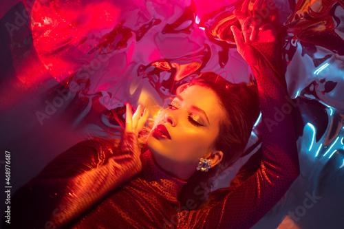Portrait of a young beautiful woman on a shimmering background, iridescent colored light, futuristic fashion shooting in neon light.