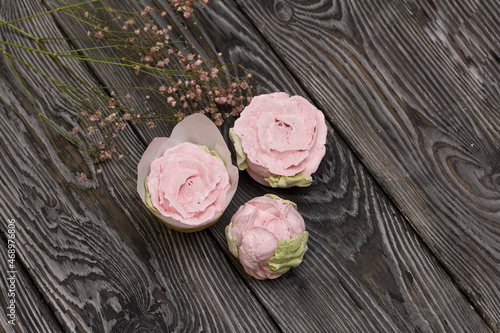 Zephyr roses. Are laid out on black pine planks. Pink flowers and green marshmallow petals are visible. Nearby is a branch of dried flowers. Close-up shot.