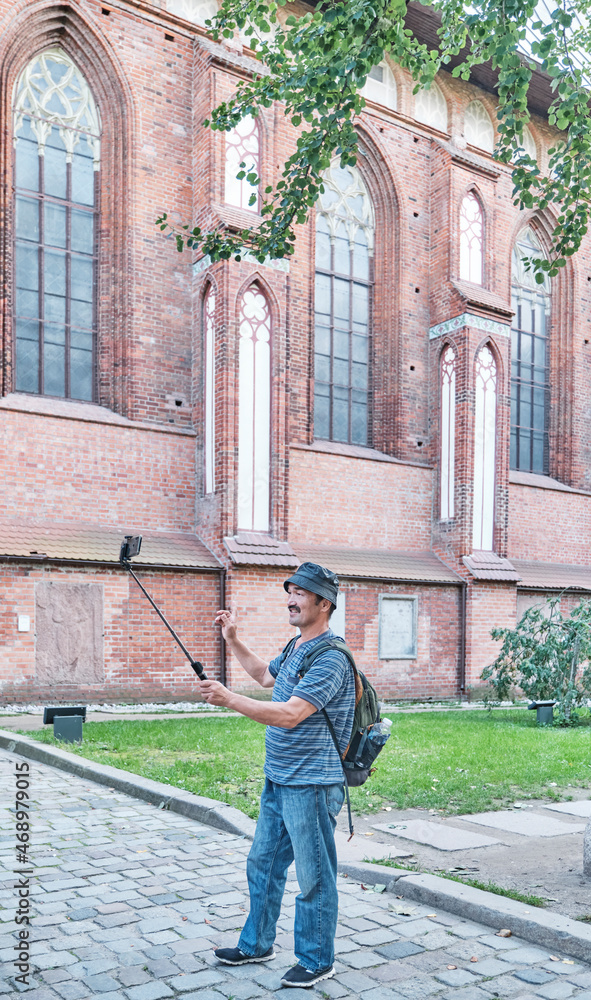 Mature Asian blogger shooting video for his blog on social network near wall of Cathedral, Kaliningrad, Russia