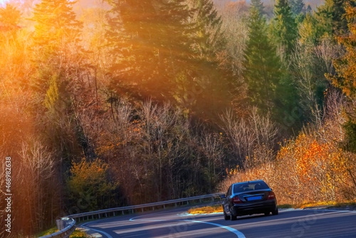 Black car on a forest road. Golden autumn. Selective focus on car. Horizontal image.