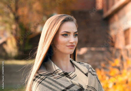 Portrait of an young attractive woman with long blonde hair enjoying her time in the autumn park with yellow trees in background