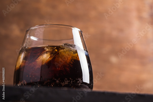 Beautiful glass with whiskey cola and ice on a dark brown wooden table background. Delicious and elegant gossed alcoholic cocktail at the bar.