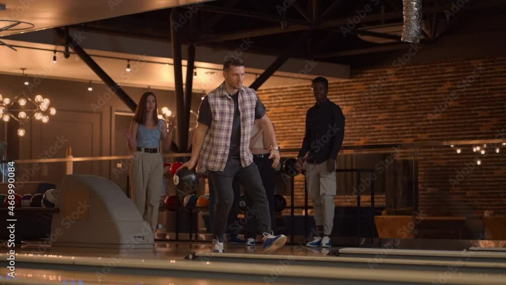 A young man throws a bowling ball and knocks out a shot with one throw and hugs and rejoices with his friends. Multi-ethnic group of friends bowling A young man throws a bowling ball and knocks out a shot with one throw and hugs and rejoices with his friends. Multi-ethnic group of friends bowling