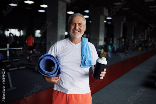 Old man with bottle of water  towel and mat in gym