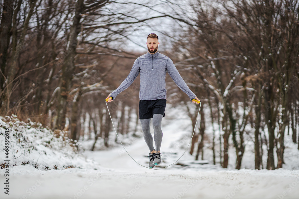 Fit sportsman jumping the rope in nature at snowy winter day. Winter fitness, cardio exercises