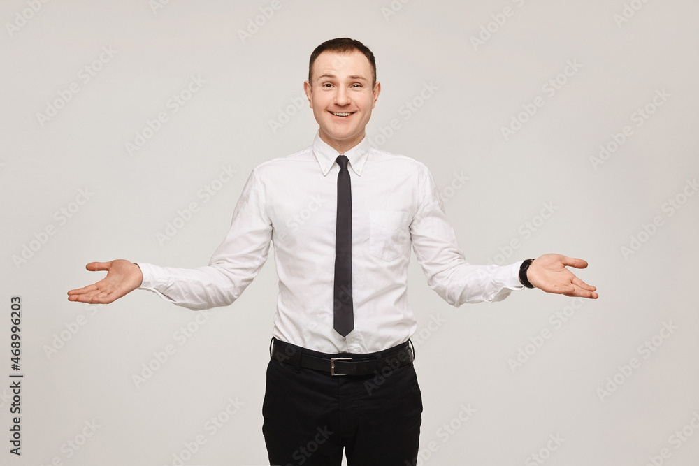 Young businessman in a white shirt and a black tie with arms spread apart on gray background. Isolated with copyspace Young businessman in a white shirt and a black tie with arms spread apart on gray background. Isolated with copyspace