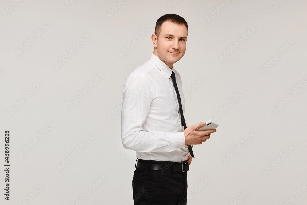A young successful man in a white shirt and a black tie keeps the phone in his hand on a gray background. Isolated with copy space A young successful man in a white shirt and a black tie keeps the phone in his hand on a gray background. Isolated with copy space