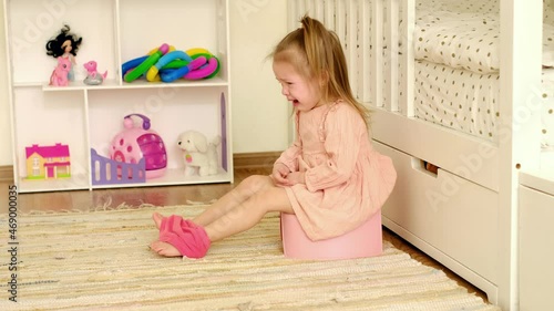 The girl is sitting on a potty in the nursery and crying bitterly. Attempts to teach the child to the toilet. Crying, tears and childish tantrums photo