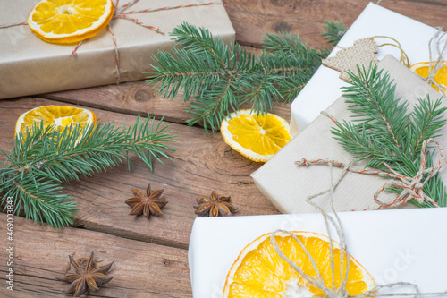 Fototapeta Naklejka Na Ścianę i Meble -  Christmas presents or gift box wrapped in kraft paper with decorations, pine cones, dry orange orange slices and fir branches on a rustic wooden background. Holiday concept