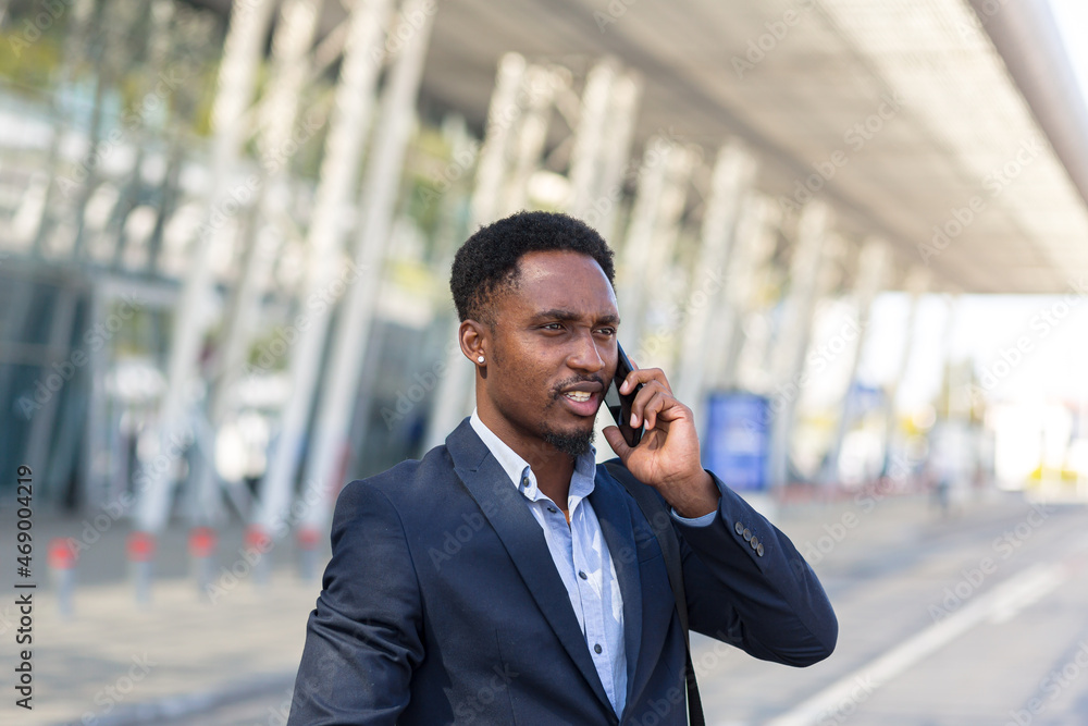 African American man talking on a cell phone near the airport, businessman arrived on a business trip African American man talking on a cell phone near the airport, businessman arrived on a business trip