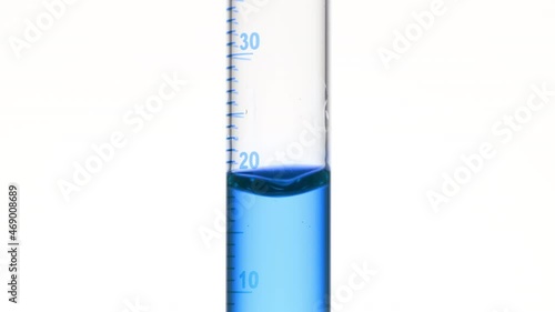Drop of blue fluid is falling down into graduated cylinder with blue transparent fluid on white background | Abstract face care cosmetics formulation concept photo