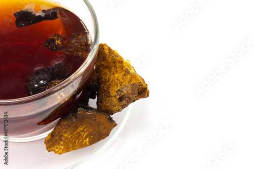 Chaga infusion with chaga mushroom pieces in a glass cup and Inonotus obliquus pieces isolated on a white background with copy space. Parasitic fungus on birch. Traditional medicine concept. Top view photo