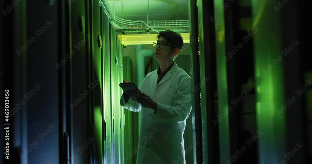 Asian male it technician in lab coat using tablet checking computer server Asian male it technician in lab coat using tablet checking computer server