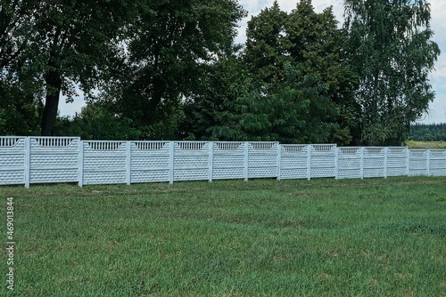 part of a long white concrete fence wall on a rural street in green grass