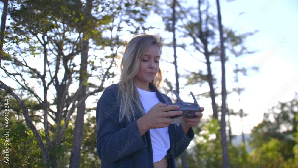 Blonde girl flying a drone, with a controller, in a mountain forest, on a sunny evening Blonde girl flying a drone, with a controller, in a mountain forest, on a sunny evening