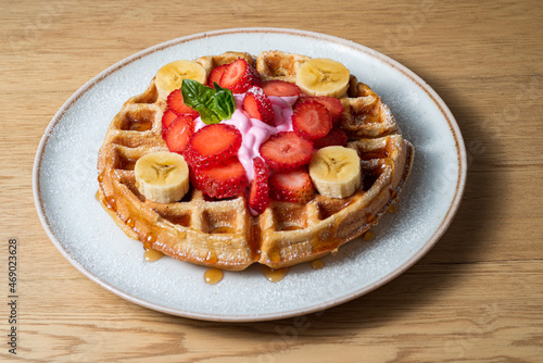 waffles on white plate, with strawberries, banana, honey and mint leaf