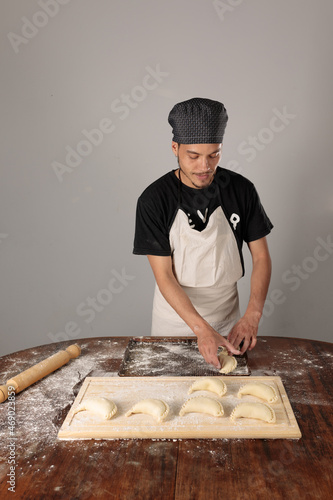 young latin american cook putting empanadas in a baking dish, for cooking. Entrepreneur. small home business