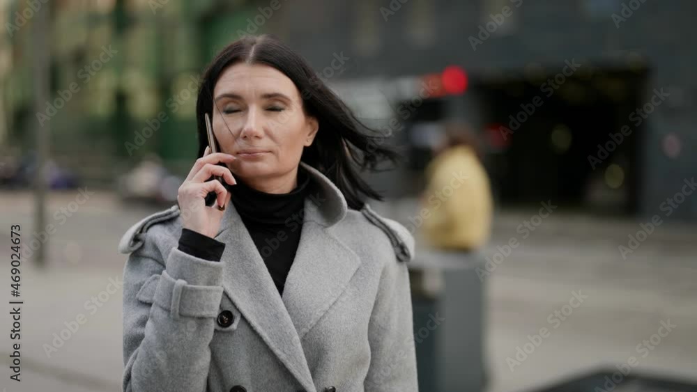 adult woman is talking by mobile phone on street in city center in autumn day adult woman is talking by mobile phone on street in city center in autumn day