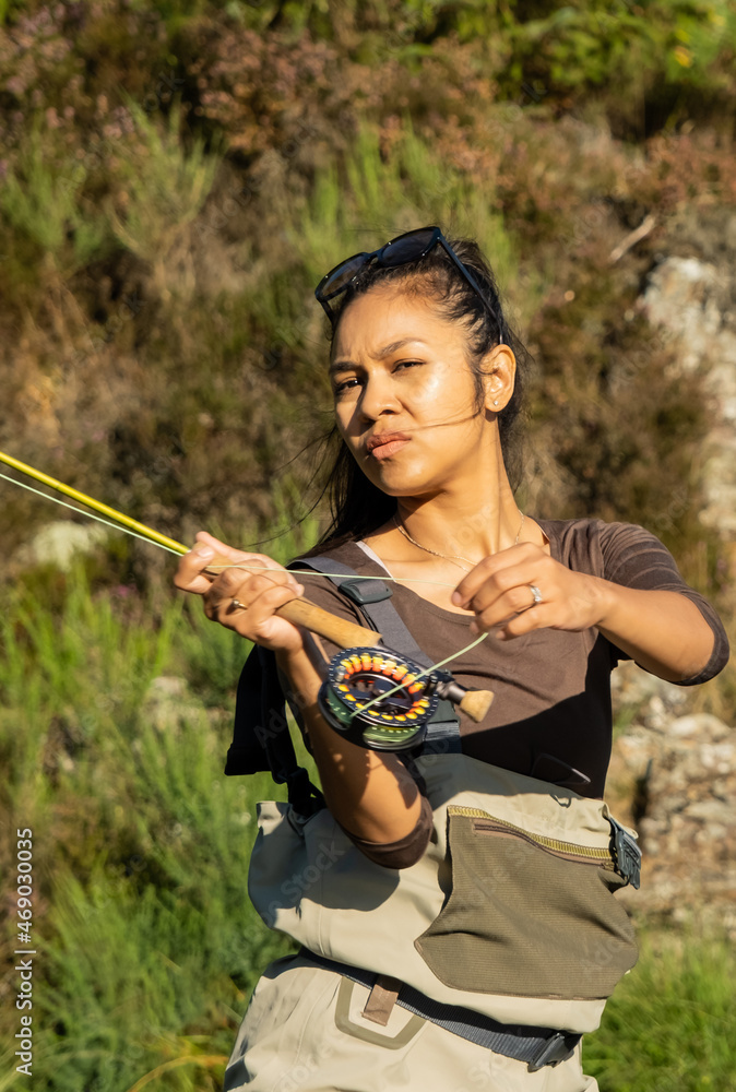 A young asian female fly fishing on a river on a summers evening