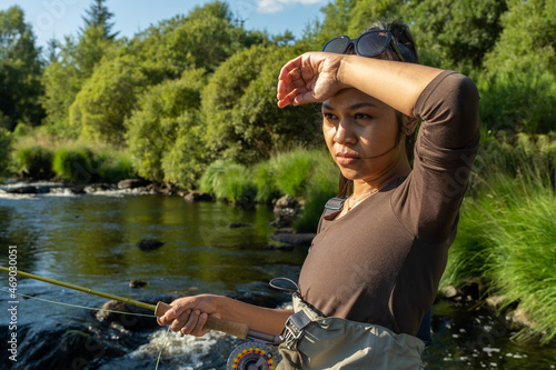 A young asian female standing fly fishing in a riffle on a river photo