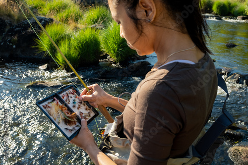 A close up of an asian female selecting fly fishing flies from a box