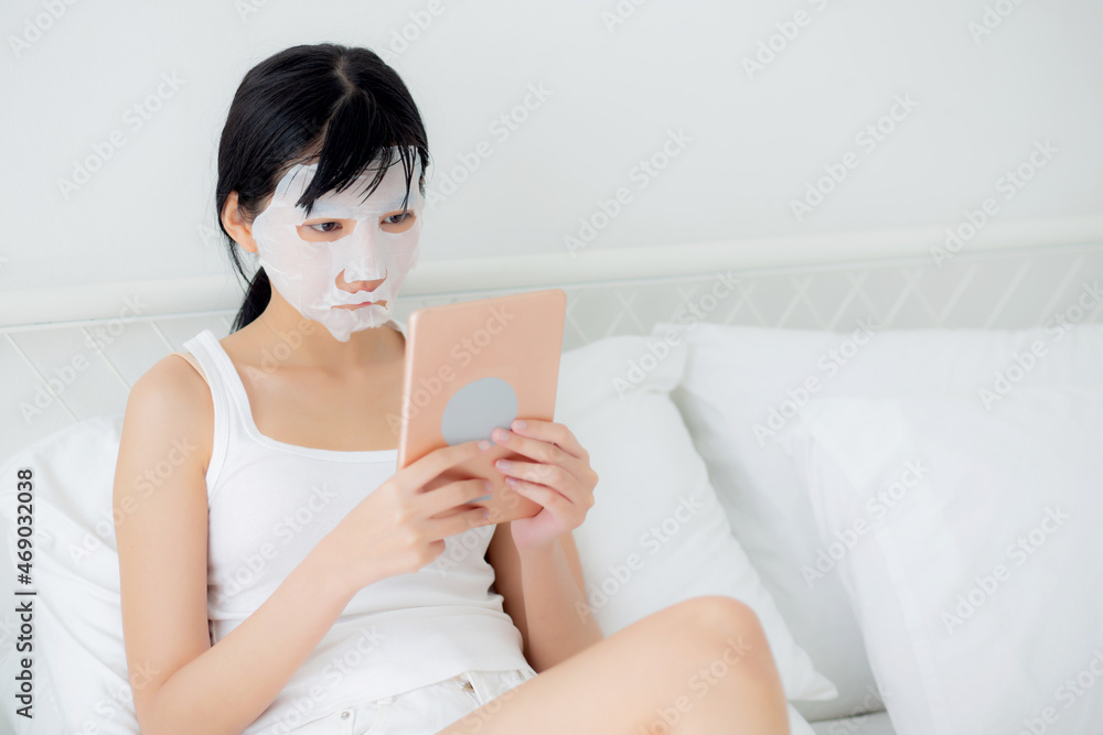 Beautiful young asian woman with sheet facial mask sitting watching tablet computer on bed at bedroom, beauty girl applying face mask for skincare of wrinkle at home, skin care, health and wellness. Beautiful young asian woman with sheet facial mask sitting watching tablet computer on bed at bedroom, beauty girl applying face mask for skincare of wrinkle at home, skin care, health and wellness.