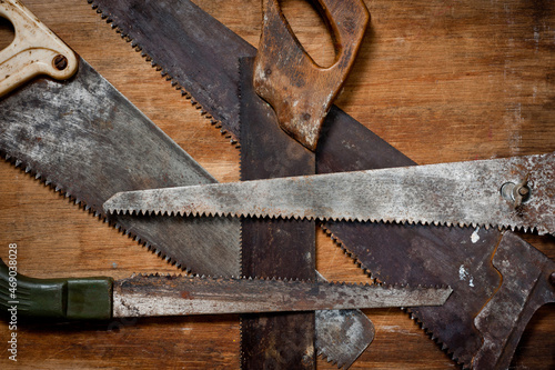 Old vintage metal saws for wood of different shapes and sizes, crumpled on a wooden background.