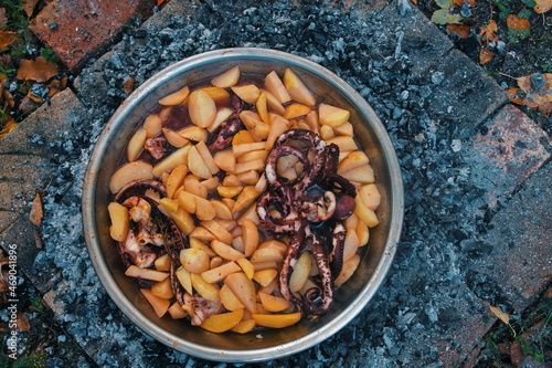 Flat lay of octopus with potatoes in metal pan on glowing firewood