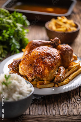 Roast chicken whole on a wooden cutting board with side dishes rice and french fries