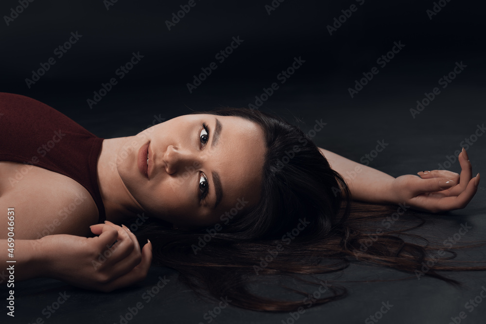 Studio photo of pretty brunette woman wearing in a black bodysuit sitting on the studio floor on black background Studio photo of pretty brunette woman wearing in a black bodysuit sitting on the studio floor on black background
