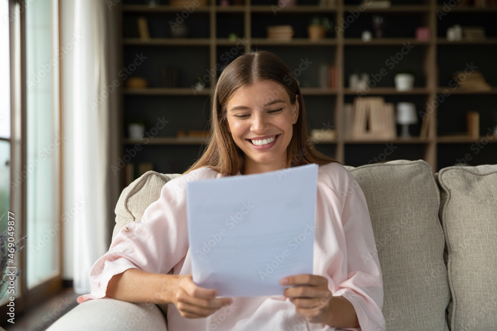 Φωτογραφία Happy young beautiful woman feeling pleased reading paper correspondence letter with good news, getting last bank mortgage payment notification or taxes refund, sitting on cozy couch at home