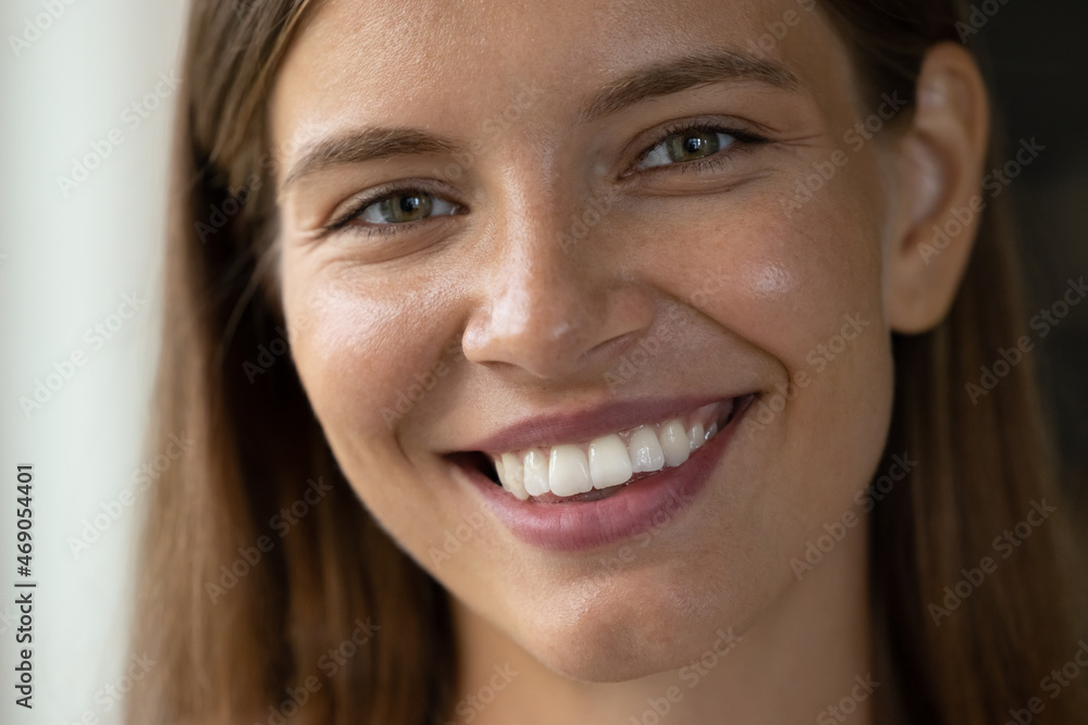 Fototapeta premium Close up head shot beautiful young woman with perfect skin looking at camera, showing whitening smile with healthy straight teeth, feeling satisfied with professional dental or cosmetology procedure.