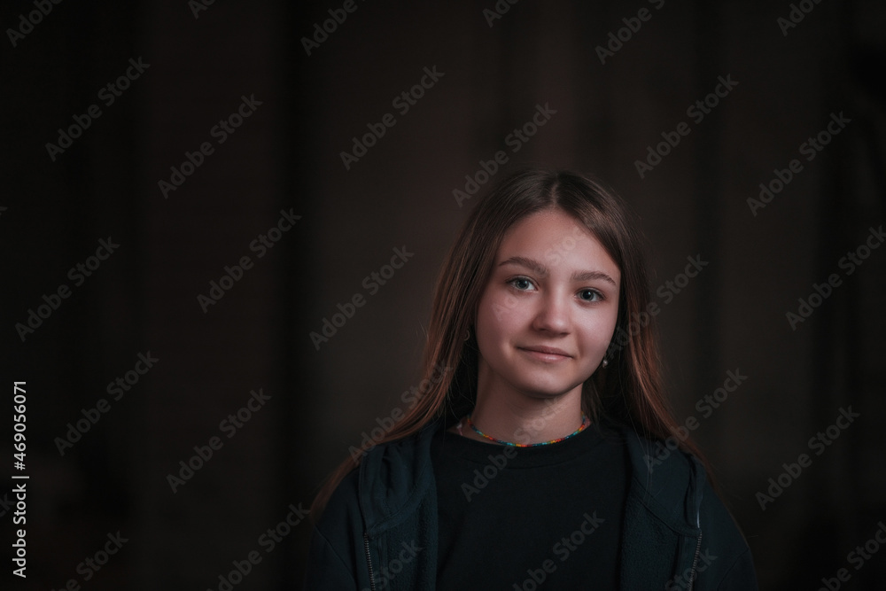 Low key portrait of a young beautiful girl in a dark room, with artistic grain and digital noise.