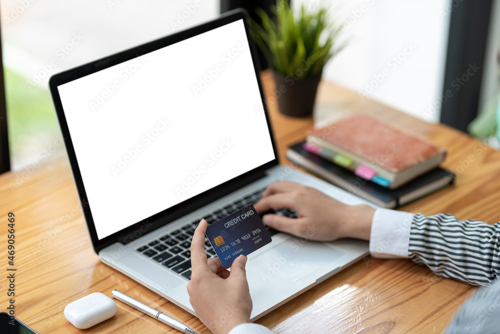 Fototapeta premium Close up of woman hands holding credit card and using laptop blank white screen. Online shopping concept.